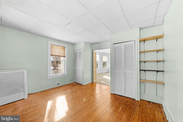 unfurnished bedroom featuring light wood-type flooring, a paneled ceiling, and two closets