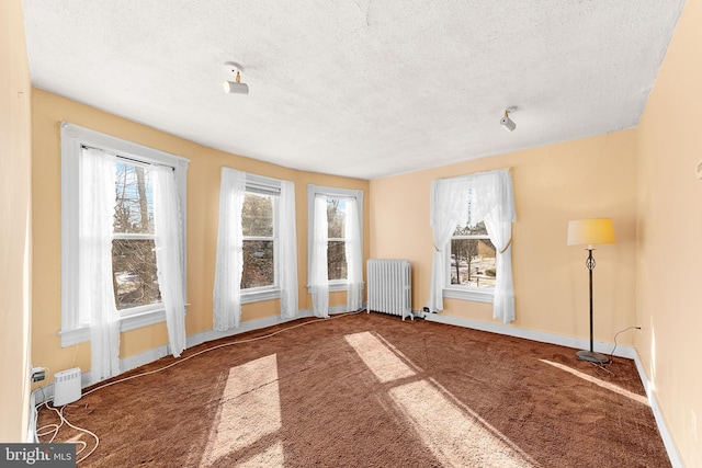 unfurnished room featuring dark colored carpet, radiator heating unit, and a textured ceiling