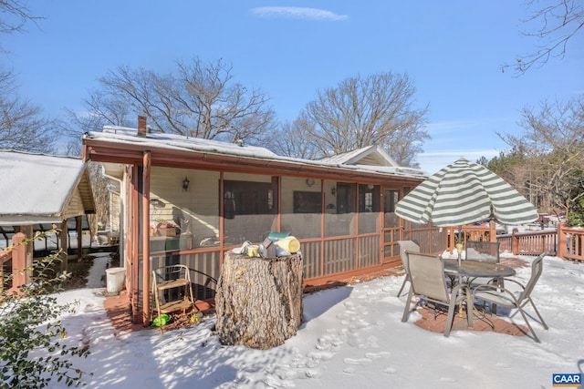 snow covered rear of property with a sunroom