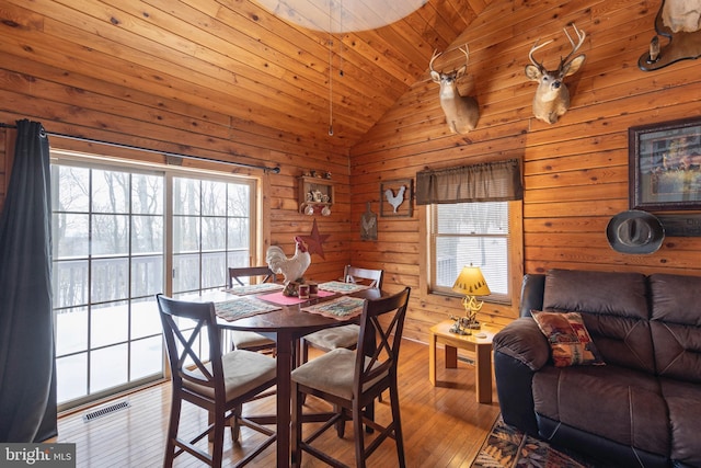 dining area with wooden walls, wooden ceiling, vaulted ceiling, and light hardwood / wood-style floors