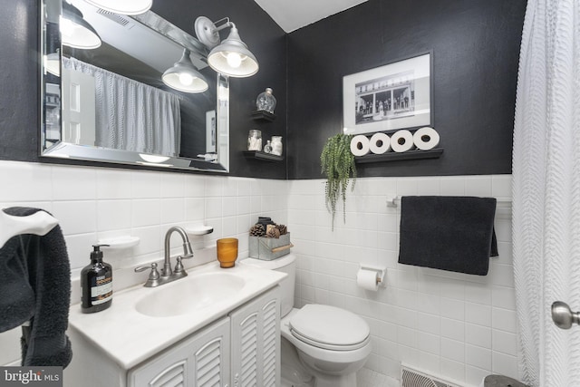 bathroom with vanity, toilet, and tile walls