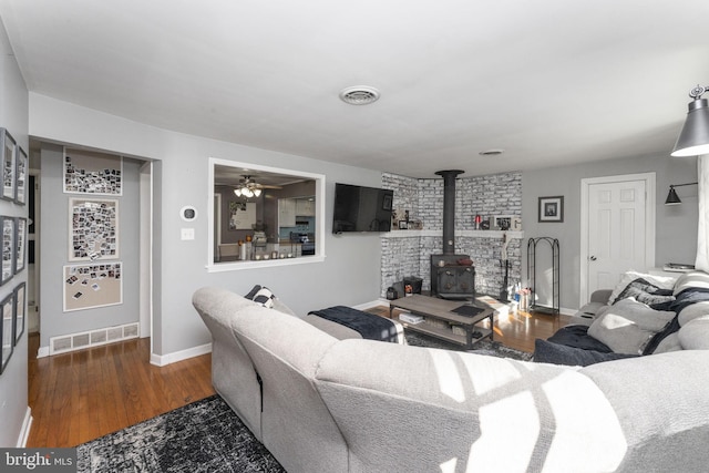 living room with dark hardwood / wood-style floors, a wood stove, and ceiling fan