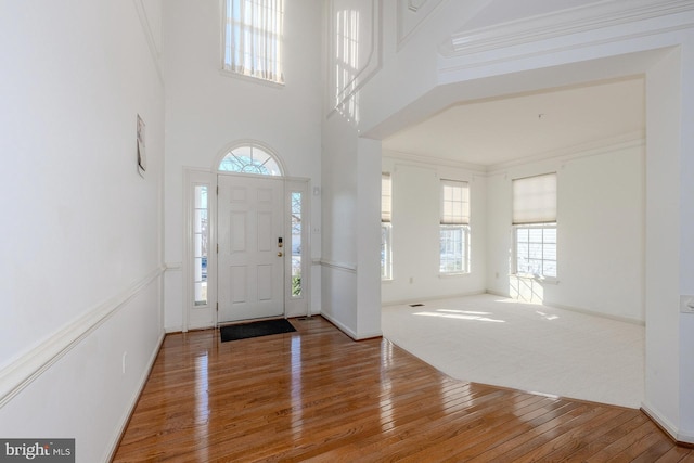 entryway with a towering ceiling, ornamental molding, and hardwood / wood-style floors