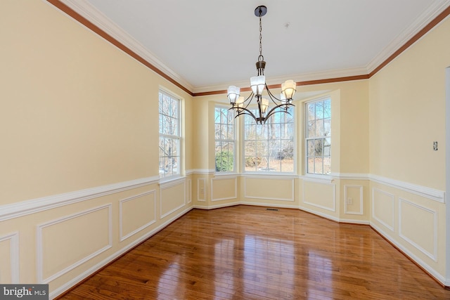 unfurnished dining area with an inviting chandelier, crown molding, and hardwood / wood-style flooring