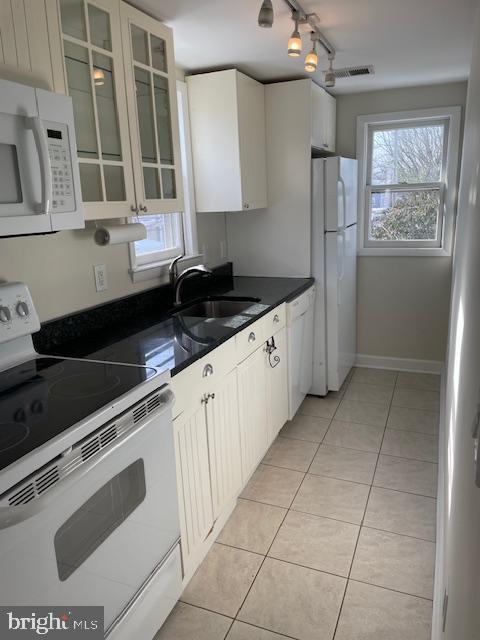 kitchen with light tile patterned floors, white appliances, white cabinetry, and sink