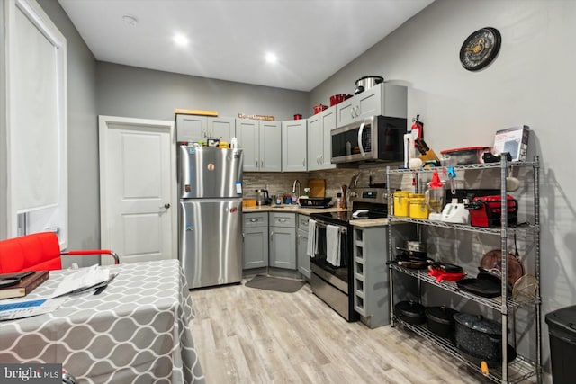 kitchen with gray cabinetry, light hardwood / wood-style flooring, appliances with stainless steel finishes, and tasteful backsplash