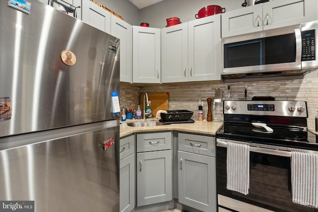 kitchen with sink, decorative backsplash, gray cabinets, appliances with stainless steel finishes, and light stone counters