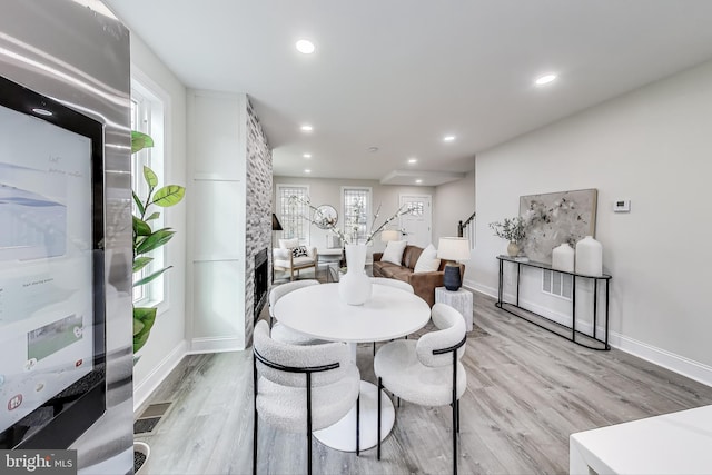 dining space featuring a stone fireplace, a healthy amount of sunlight, and light hardwood / wood-style floors