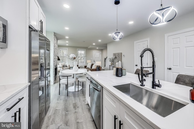 kitchen featuring sink, stainless steel appliances, pendant lighting, white cabinets, and light wood-type flooring