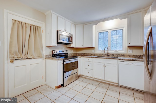 kitchen with white cabinets, sink, dark stone countertops, light tile patterned floors, and appliances with stainless steel finishes