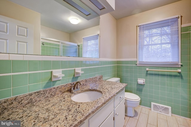 bathroom featuring vanity, a shower with door, plenty of natural light, and tile walls