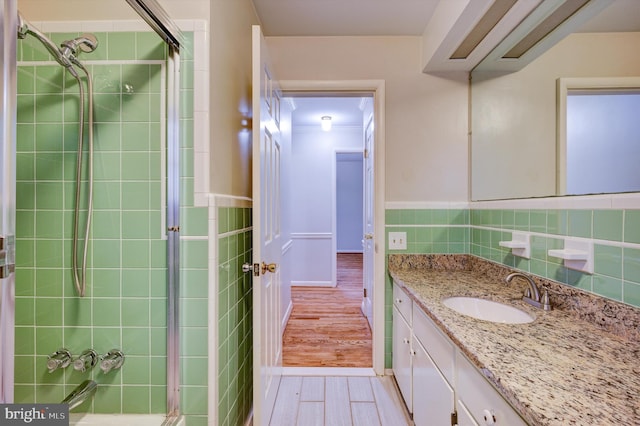 bathroom with hardwood / wood-style floors, vanity, a shower with shower door, and tile walls