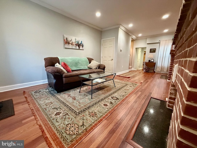 living room with hardwood / wood-style floors, ornamental molding, and a brick fireplace