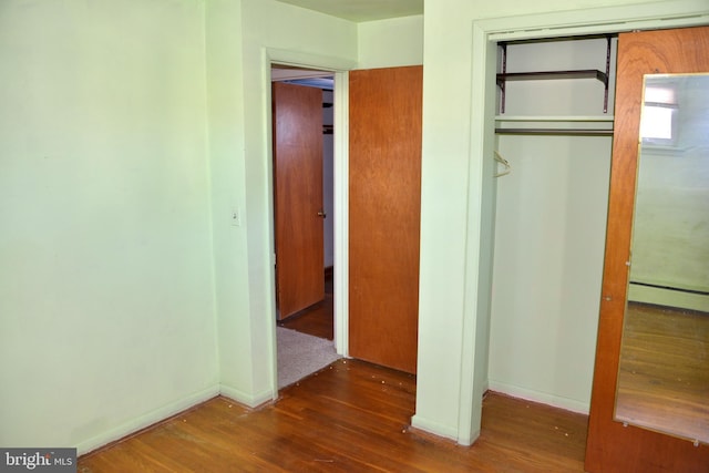 unfurnished bedroom with a baseboard heating unit, a closet, and dark wood-type flooring