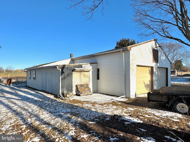 snow covered house with an outdoor structure and a garage