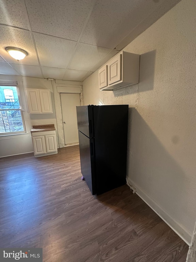 kitchen featuring a paneled ceiling, black fridge, white cabinetry, and dark wood-type flooring