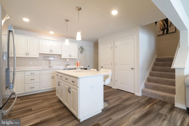 kitchen with dark wood-type flooring, stainless steel fridge, decorative light fixtures, a kitchen island, and white cabinetry