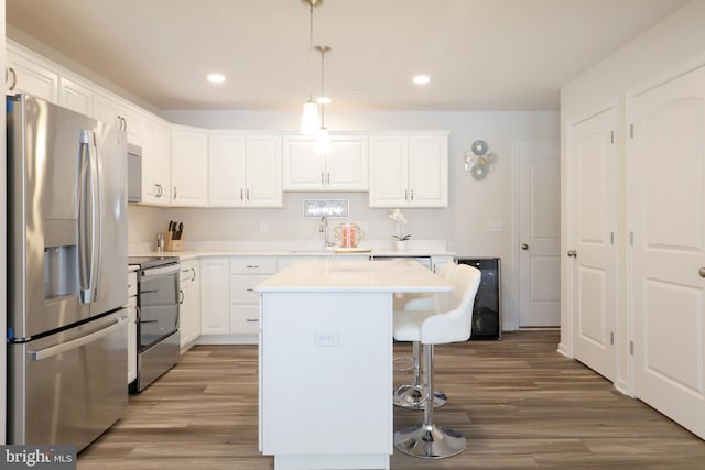 kitchen featuring a center island, hanging light fixtures, stainless steel appliances, wood-type flooring, and white cabinets