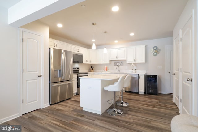 kitchen featuring pendant lighting, appliances with stainless steel finishes, a kitchen island, white cabinetry, and beverage cooler