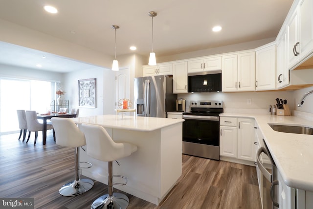 kitchen featuring stainless steel appliances, sink, white cabinets, a center island, and hanging light fixtures