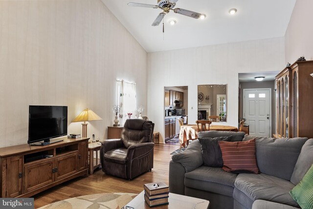 living room with ceiling fan, light wood-type flooring, and high vaulted ceiling