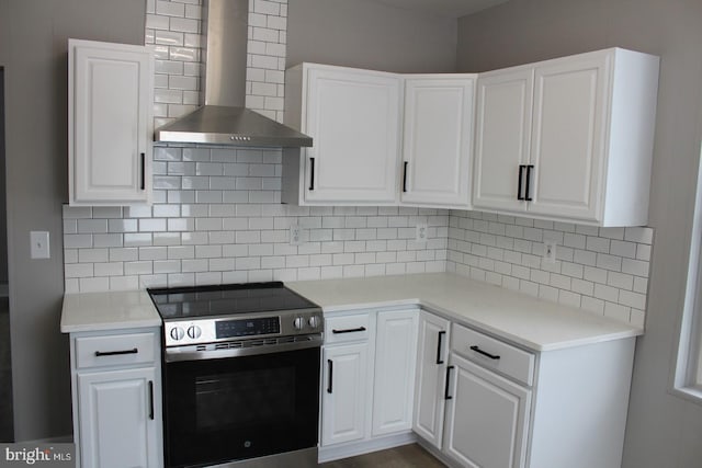 kitchen with decorative backsplash, stainless steel electric range, white cabinetry, and wall chimney range hood