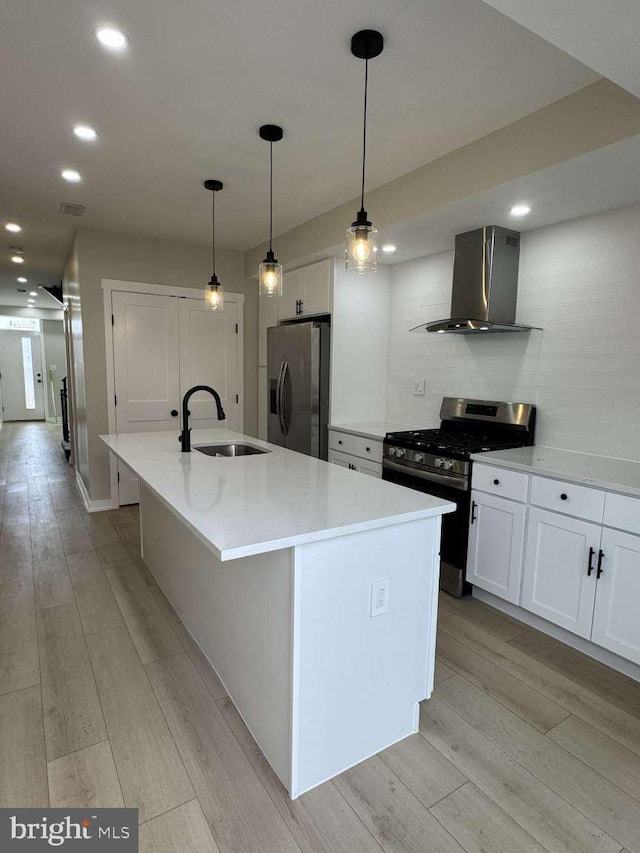 kitchen with a center island with sink, sink, white cabinetry, appliances with stainless steel finishes, and wall chimney exhaust hood