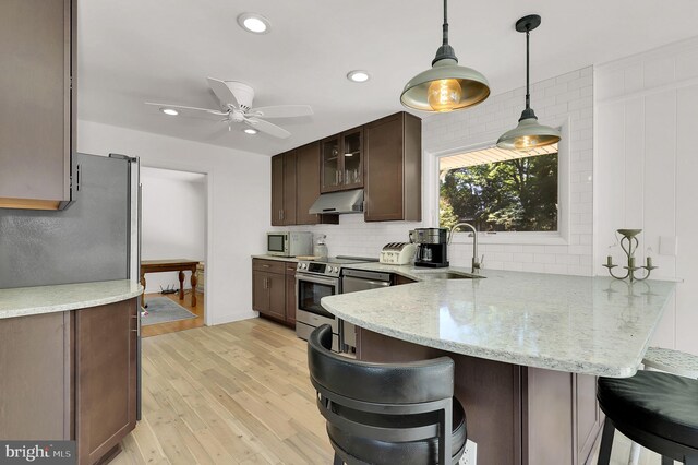 kitchen with a sink, stainless steel appliances, under cabinet range hood, a peninsula, and tasteful backsplash