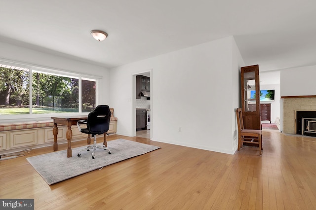 home office with light wood-type flooring, a fireplace, and baseboards