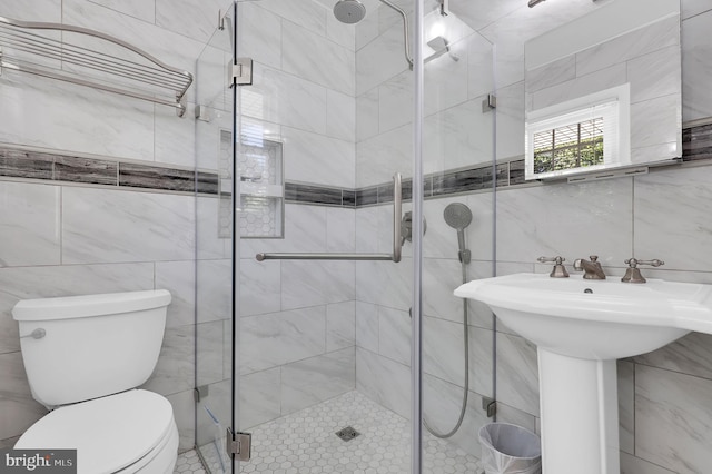 bathroom with tile walls, a shower stall, toilet, and a sink