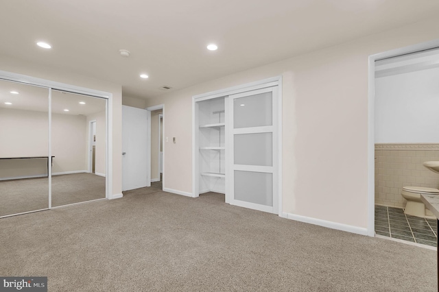 unfurnished bedroom featuring two closets, carpet floors, recessed lighting, ensuite bath, and tile walls