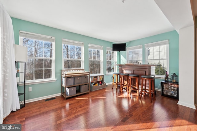 living area featuring a dry bar, wood-type flooring, visible vents, and a healthy amount of sunlight