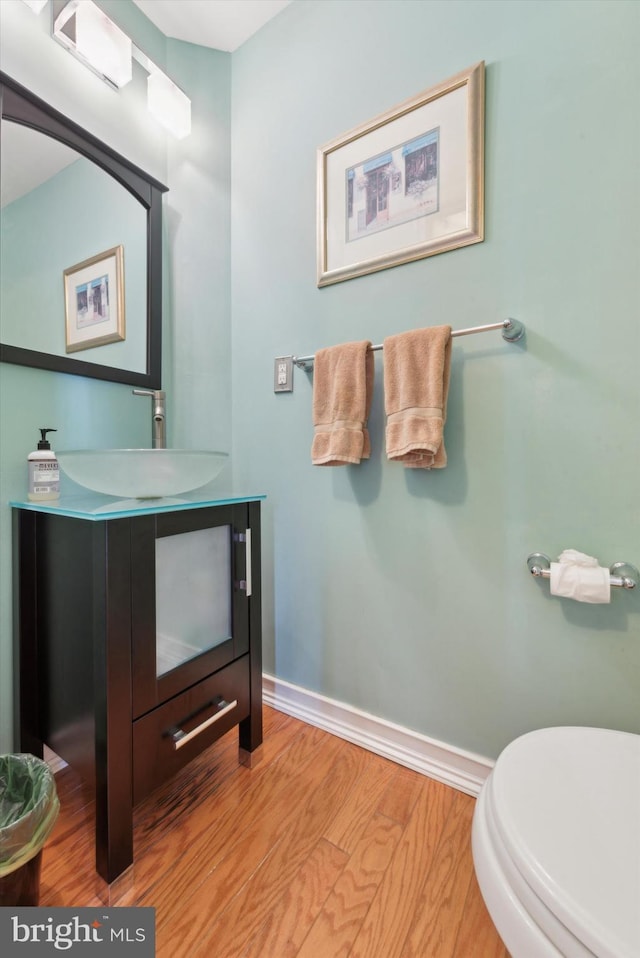 bathroom with toilet, vanity, baseboards, and wood finished floors