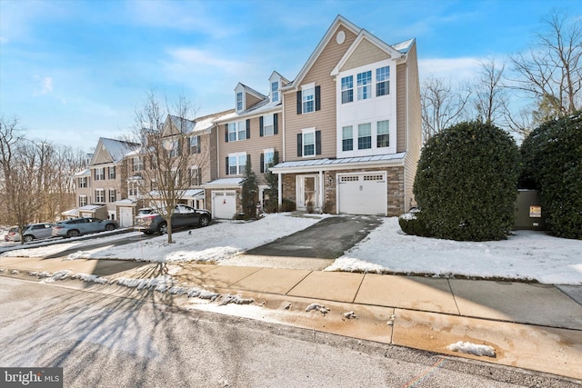 townhome / multi-family property featuring an attached garage, stone siding, a residential view, and aphalt driveway