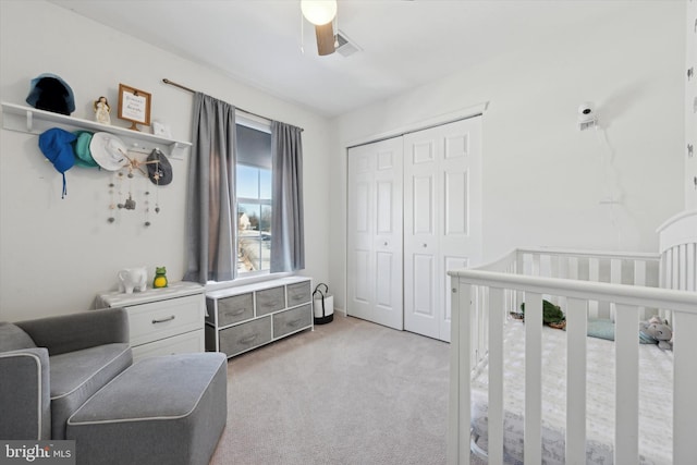 bedroom featuring light carpet, ceiling fan, a closet, and a nursery area