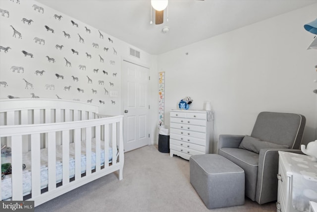 carpeted bedroom featuring a crib, visible vents, and a ceiling fan