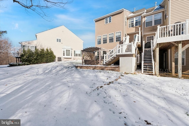 snow covered back of property with a deck and stairway