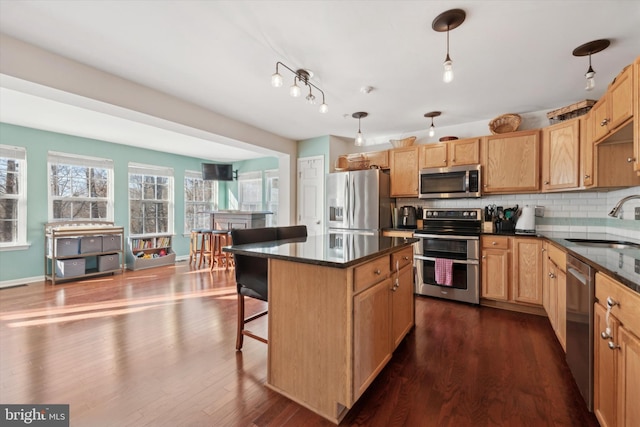 kitchen with stainless steel appliances, a breakfast bar, a sink, decorative backsplash, and dark wood-style floors