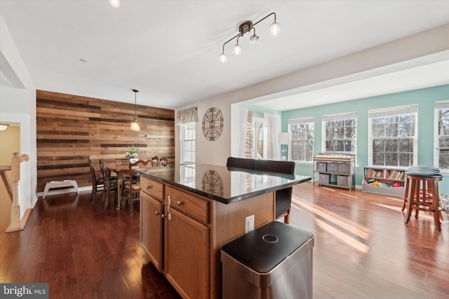 kitchen with hanging light fixtures, dark wood-type flooring, a center island, and wooden walls