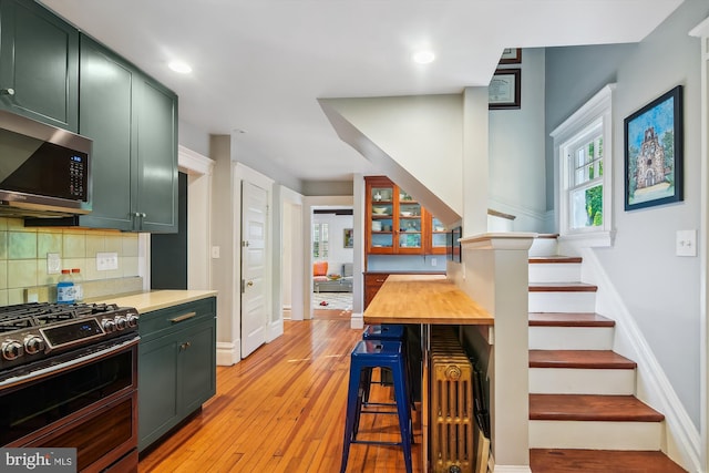 kitchen featuring a kitchen bar, stainless steel appliances, backsplash, green cabinetry, and light hardwood / wood-style flooring