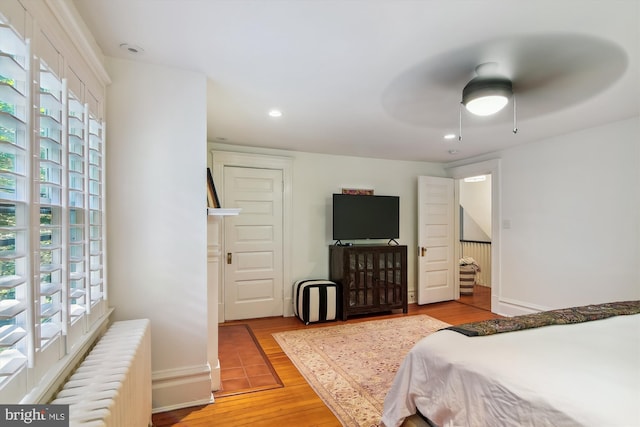 bedroom with ceiling fan, light wood-type flooring, radiator heating unit, and multiple windows