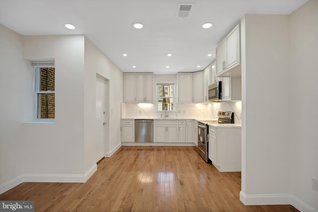 kitchen featuring white cabinetry, sink, tasteful backsplash, light hardwood / wood-style flooring, and appliances with stainless steel finishes