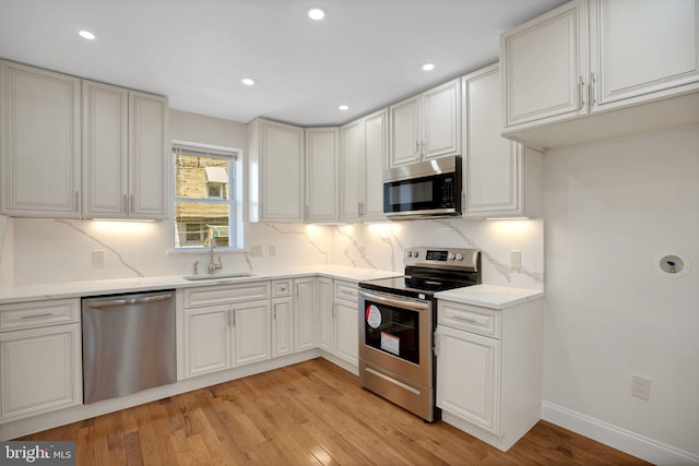 kitchen featuring sink, stainless steel appliances, decorative backsplash, white cabinets, and light wood-type flooring