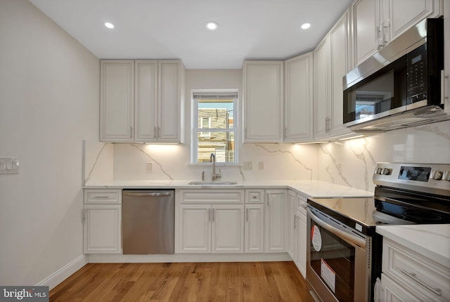 kitchen with sink, white cabinetry, stainless steel appliances, and light hardwood / wood-style flooring