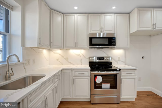 kitchen featuring light stone countertops, sink, backsplash, white cabinets, and appliances with stainless steel finishes