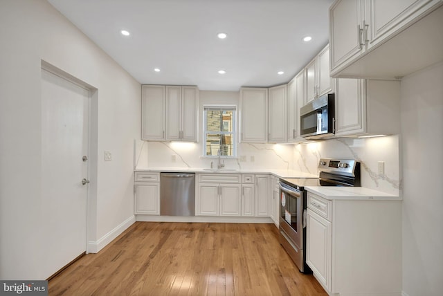 kitchen featuring appliances with stainless steel finishes, tasteful backsplash, sink, light hardwood / wood-style flooring, and white cabinets