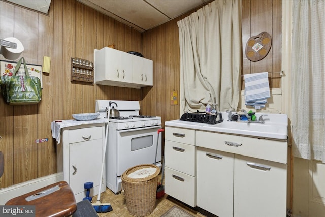 kitchen with white cabinets, white gas range oven, wooden walls, and sink