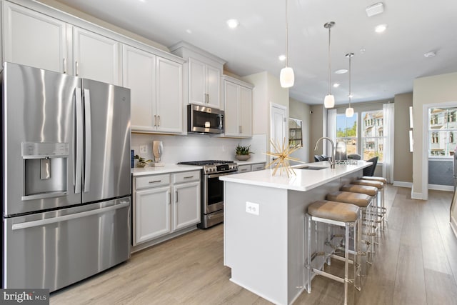 kitchen featuring white cabinets, hanging light fixtures, stainless steel appliances, and a kitchen island with sink