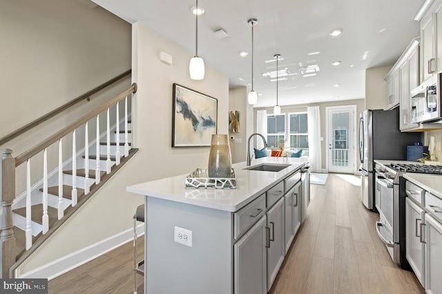 kitchen with sink, hanging light fixtures, an island with sink, appliances with stainless steel finishes, and light wood-type flooring