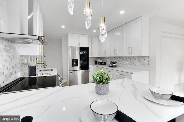 kitchen featuring wall chimney range hood, stainless steel fridge with ice dispenser, tasteful backsplash, light stone counters, and white cabinetry